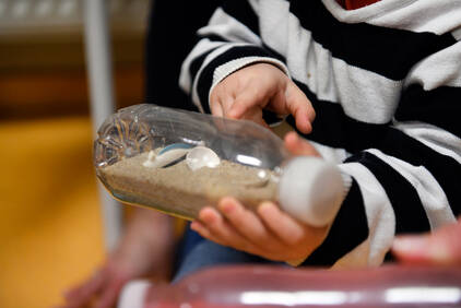 Photo d'un enfant jouant avec une bouteille remplit de sable et jouets